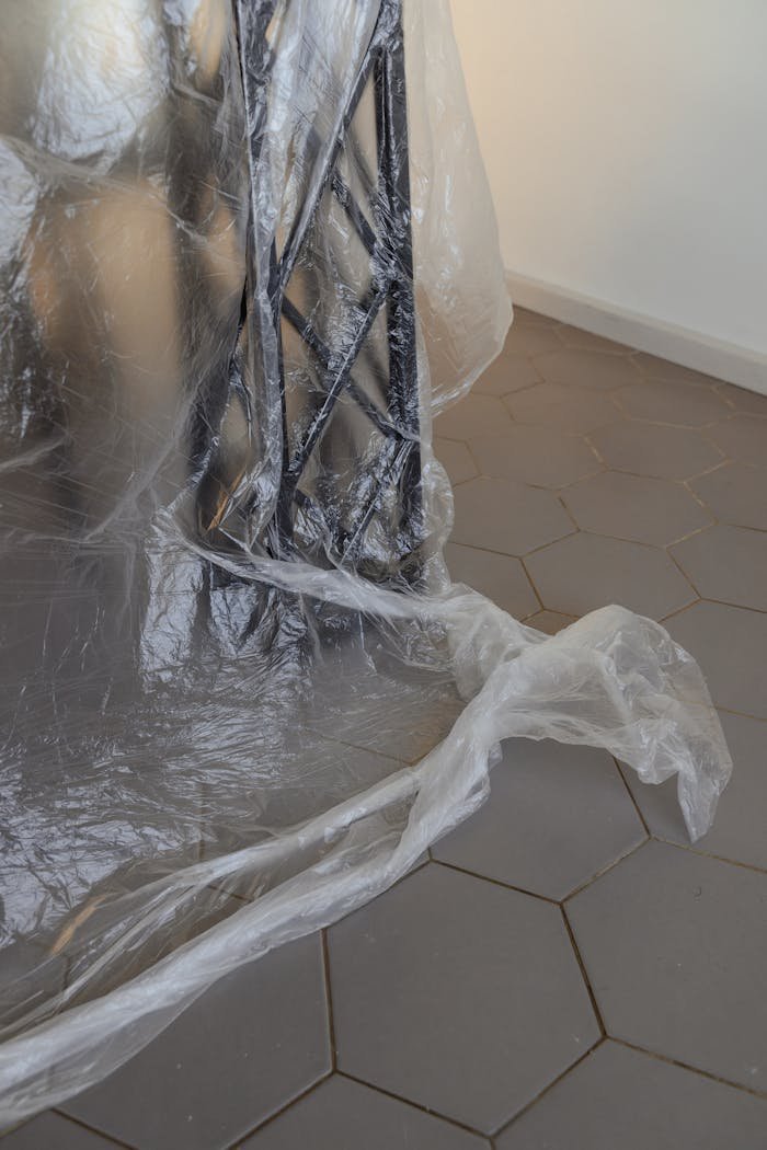 Close-up of furniture wrapped in plastic on indoor hexagonal tile flooring.